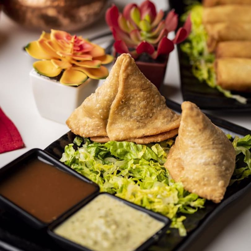 Crispy golden samosas on a bed of lettuce with two dipping sauces, at India Bistro.