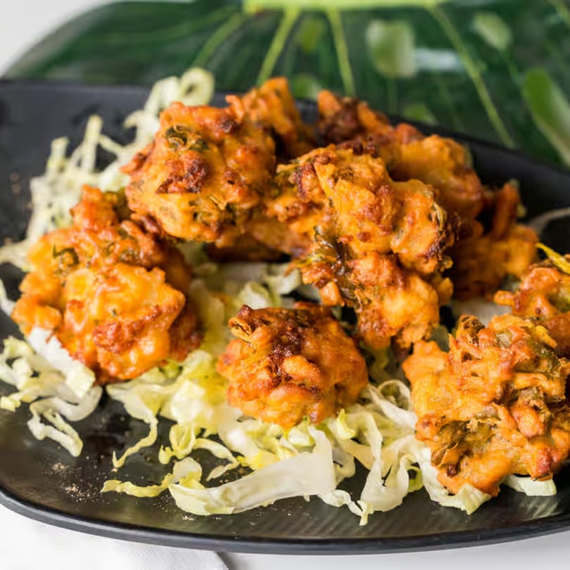 Crispy golden-brown Indian pakoras, garnished with shredded cabbage, on a black plate.